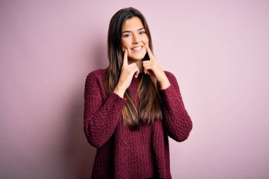 İzole edilmiş pembe arka planda sıradan bir süveter giyen genç ve güzel bir kız ağzı açık gülümseyen, parmakları açık ve neşeli gülümsemeye zorlayan.