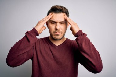Mavi gözlü genç adam izole edilmiş arka planda dikilip acı ve migren yüzünden çaresiz ve stresli bir şekilde acı çekiyor. Ellerini başının üstüne koy..