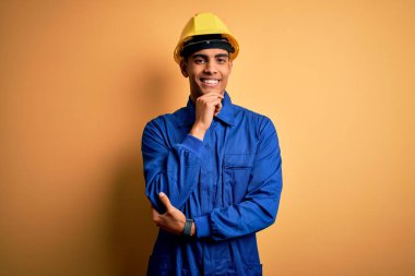 Mavi üniforma giyen ve güvenlik kaskı takan genç ve yakışıklı Afro-Amerikan işçi kameraya kollarını kavuşturup elleriyle çenesini kaldırarak gülümsüyor. Olumlu düşünüyorum..