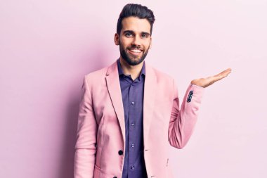 Sakallı, zarif ceketli, neşeli gülümseyen, eli avucunda kameraya bakan genç yakışıklı bir adam.. 