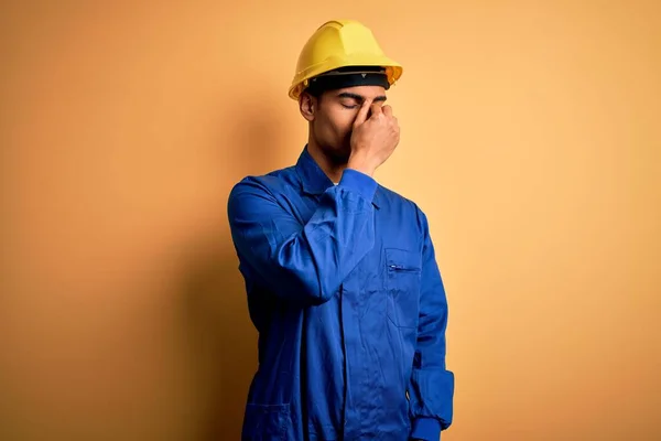 青い制服とセキュリティヘルメット疲れ摩擦鼻や目疲労や頭痛を感じる若いハンサムなアフリカ系アメリカ人労働者の男 ストレスとフラストレーションの概念 — ストック写真
