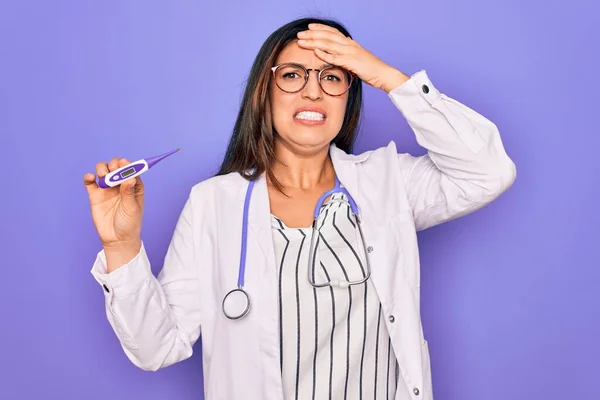 紫色の背景の上に医療用温度計を示す専門家の医師の女性は 恥と驚きの顔でショックを受け 怒っていると不満を手で強調した 恐怖と過ちへの動揺 — ストック写真