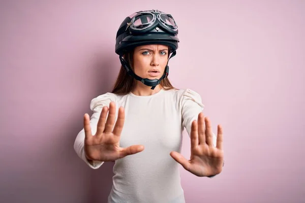 若いです美しいですオートバイの女性とともに青い目ピンクの背景に元ヘルメットを身に着けています手掌で停止ジェスチャーを行います 怒っていると欲求不満式 — ストック写真