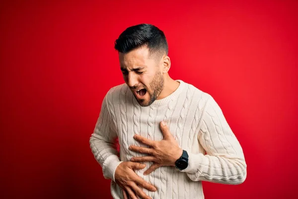 stock image Young handsome man wearing casual white sweater standing over isolated red background with hand on stomach because nausea, painful disease feeling unwell. Ache concept.