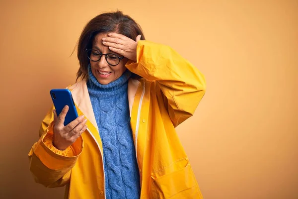 Žena Středního Věku Žlutém Plášti Používající Smartphone Izolovaném Žlutém Pozadí — Stock fotografie