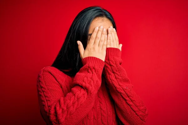 Young beautiful asian woman wearing casual sweater standing over isolated red background with sad expression covering face with hands while crying. Depression concept.