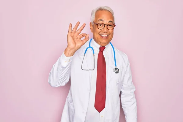 手と指でOkサインを行う肯定的な笑みを浮かべて聴診器とプロの医療コートを身に着けている中世のシニア白髪の医師の男 成功した表現 — ストック写真