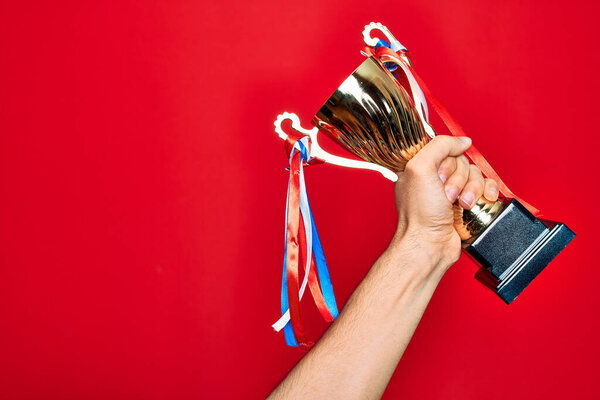 Beautiful hand of man holding golden trophy cup over isolated red background