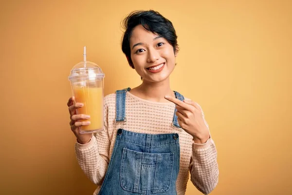 아름다운 여자가 오렌지 주스를 마시고 있습니다 위에서 손가락으로 행복하게 가리키고 — 스톡 사진