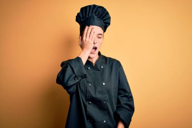 Aşçı üniforması giyen güzel bir kadın ve sarı arka planda duran bir şapka takan esneyen yorgun bir kadın. Yüzün yarısını, gözünü ve ağzını eliyle kapatıyor. Yüzüm acıyor..