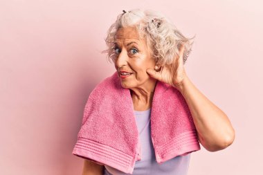 Kıdemli gri saçlı kadın spor giysisi ve havlu giymiş kulaklarında gülümseyerek dedikodu ya da dedikoduları dinliyor. Sağırlık kavramı. 