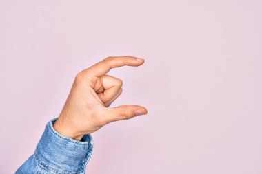 İzole edilmiş pembe arka plan üzerinde parmaklarını gösteren beyaz bir adamın eli. Görünmez bir şeyi alıp, parmaklarıyla uzayı gösteren bir nesneyi tutuyor.