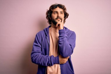 Genç, yakışıklı, sakallı, pembe arka planda sıradan bir kazak giyen, eli çenesinde soru soran, düşünceli bir adam. Gülen ve düşünceli bir yüz. Şüphe kavramı.