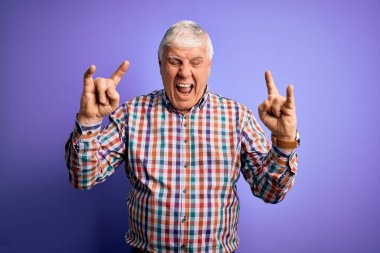 Ayrı mor arka plan üzerine sıradan bir tişört giyen yaşlı yakışıklı beyaz adam çılgın bir ifadeyle elleri havada rock sembolü yaparak bağırıyor. Müzik yıldızı. Ağır müzik konsepti.