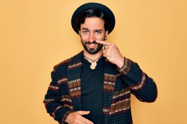 Genç, yakışıklı, bohem, hippi tarzı giyinmiş ve bohem şapkalı, el ve burunla işaret eden neşeli bir adam. Güzellik konsepti