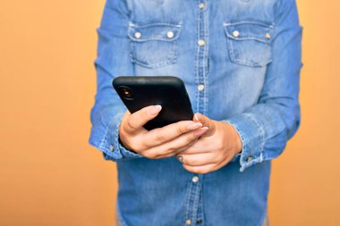 Genç beyaz kadın, izole edilmiş sarı arka plan üzerinde akıllı telefon kullanarak konuşuyor.