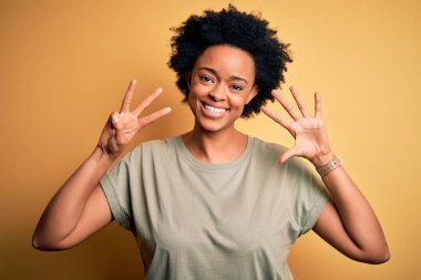 Kıvırcık saçlı, gündelik tişörtlü, genç ve güzel Afro-Amerikan kadın 8 numaralı parmaklarını gösterirken kendinden emin ve mutlu bir şekilde gülümsüyor..