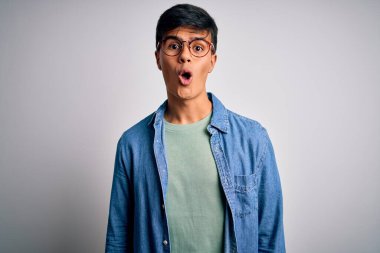 Genç, yakışıklı bir adam, gözlüklü, sıradan bir gömlek ve gözlüklü, izole edilmiş beyaz bir arka planda, korkmuş ve şok olmuş bir halde..