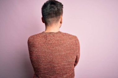 Pembe izole arka plan üzerine sıradan bir kazak giyen yakışıklı beyaz bir adam kollarını kavuşturup arkaya bakıyor.