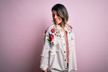 Moda kıyafetleri giyen genç ve güzel bir kadın. Manken, sokak tarzı giyiniyor. Pembe arka planda dikiliyor.