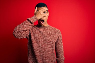 Genç, yakışıklı, Afro-Amerikalı bir adam kırmızı arka planda dikilmiş utangaç bir ifadeyle parmaklarının arasından bakarken, yüzünü ve gözlerini kapatan kırmızı arka planda dikiliyor..