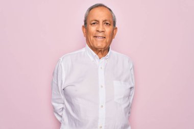 Üst düzey yakışıklı, gri saçlı, zarif tişörtlü, soyutlanmış pembe arka planda, yüzünde mutlu ve havalı bir gülümseme olan bir adam. Şanslı kişi..