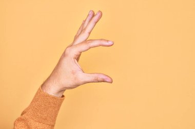 İzole edilmiş sarı arka plan üzerinde parmaklarını gösteren beyaz bir adamın eli. Görünmez bir şeyi alıp, parmaklarıyla uzayı gösteren bir nesneyi tutuyor.
