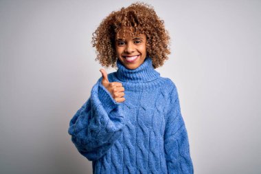 Genç ve güzel Afro-Amerikan kadın balıkçı yaka kazak giyip beyaz arka planda mutlu bir el hareketi yapıyor. Kameraya bakıp başarıyı gösteren ifade onaylanıyor.