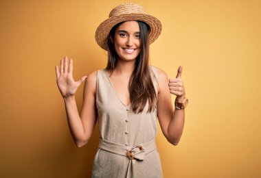 Genç ve güzel esmer kadın tatilde. Sıradan elbiseler ve şapkalar giyiyor. Altıncı parmaklarıyla işaret ediyor ve gülümsüyor..