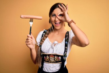 Genç esmer Alman kadın geleneksel Ekim Festivali elbisesi giyiyor. Elinde gülen yüzlü sosis var. Tamam.