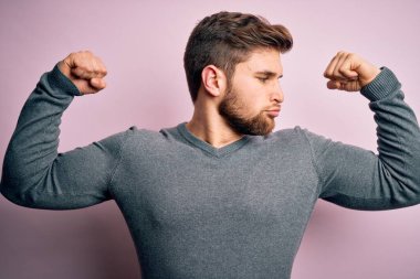 Sakallı, mavi gözlü, sıradan süveter giyen ve kollarında gururla gülümseyen genç sarışın adam. Fitness konsepti.