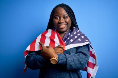 Genç vatansever Afro-Amerikan artı örgülü kadın. Birleşik Devletler bayrağı takıyor. El ve parmaklarıyla işaret ederek çok mutlu.