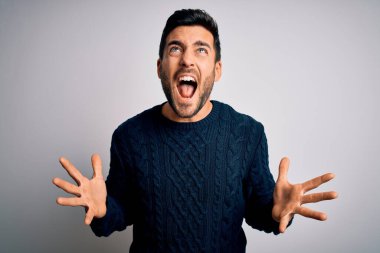 Sakallı, sıradan bir süveter giyen genç ve yakışıklı bir adam beyaz arka plan üzerinde deli deli deli bağırıyor ve agresif bir ifade ve kollar havada bağırıyor. Hayal kırıklığı konsepti.