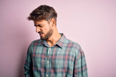 Sakallı genç yakışıklı bir adam pembe arka plan üzerinde duruyor. Midesi bulanıyor ve acı çekiyor. Ache kavramı.