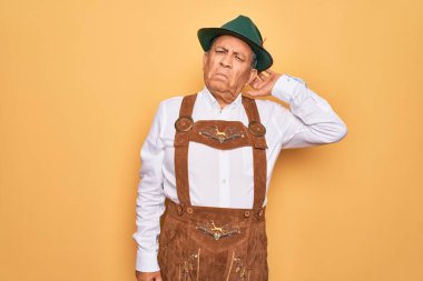 Sarı arka planda Alman geleneksel ahşap şenliği kıyafeti giyen yaşlı gri saçlı adam soru sormayı merak ediyor. Şüpheyle kararsız, kafa kafaya düşünerek. Düşünceli kavram.