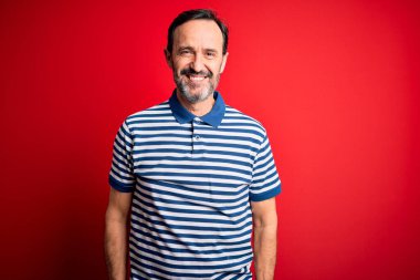 Yüzünde mutlu ve havalı bir gülümsemeyle izole edilmiş kırmızı arka planda duran sıradan çizgili polo giyen orta yaşlı beyaz bir adam. Şanslı kişi..