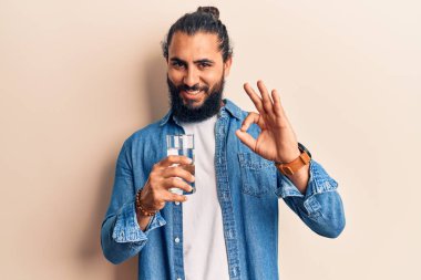 Genç Arap adam bir bardak su içiyor. Parmaklarıyla imza atıyor. Gülümsüyor. 