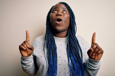 Beyaz arka planda sıradan bir kazak giyen Afrikalı Amerikalı artı cüsseli kadın şaşkın şaşkın yukarı bakıyor, parmaklarıyla işaret ediyor ve kollarını kaldırıyordu..