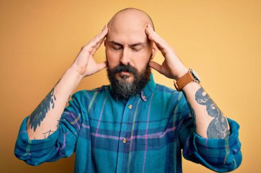 Sakallı, sakallı, sıradan bir adam izole edilmiş sarı arka planda dikiliyor. Ağrı ve migrenden dolayı baş ağrısı ve stresten muzdarip. Ellerini başının üstüne koy..
