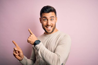 Soyutlanmış pembe arka planda dikilen sıradan bir süveter giyen genç yakışıklı. Gülümsüyor ve kameraya bakıyor. İki eliyle ve parmaklarıyla kenarı işaret ediyor..