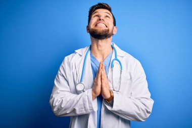 Sakallı, mavi gözlü, beyaz önlüklü, steteskoplu genç sarışın doktor elleri bağlı yalvarıyor ve dua ediyor. Yüzünde umut ifadesi var. Çok duygusal ve endişeli. Yalvarıyorum..