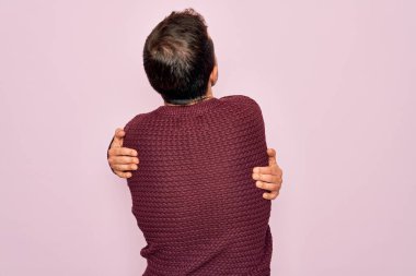 Mavi gözlü, pembe arka planda sıradan bir süveter giyen, mutlu ve pozitif bir şekilde sarılan genç, yakışıklı bir adam. Sevgi ve özgüven.