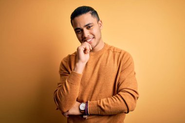 İzole edilmiş sarı arka planda dikilen sıradan süveter giyen genç Brezilyalı adam çapraz kollar ve çeneyle gülümseyen kameraya bakıyor. Olumlu düşünüyorum..