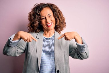 Orta yaşlı, güzel iş kadını zarif bir ceket giyiyor pembe arka planda kendine güvenen, yüzünde bir gülümsemeyle, gururlu ve mutlu bir şekilde kendini gösteren..