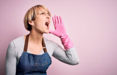 Sarışın, kısa saçlı, önlüklü, pembe arka planda eldivenleri olan genç, temiz bir kadın el ele tutuşarak bağırıyor ve bağırıyordu. İletişim konsepti.