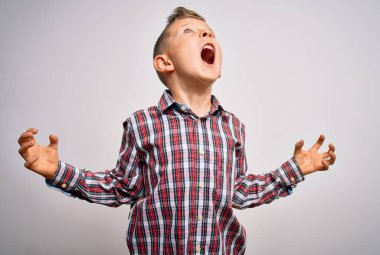 Mavi gözlü, zarif gömlekli küçük beyaz bir çocuk izole arka planda duruyor deli deli deli bağırıyor ve agresif bir ifadeyle ve kollarıyla bağırıyor. Hayal kırıklığı konsepti.