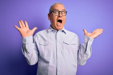 Orta yaşlı, beyaz, çizgili gömlek ve mor arka planda gözlük takan yakışıklı adam çılgın ve başarıyı kollarını kaldırıp heyecanla haykırarak kutluyor. Kazanan konsept