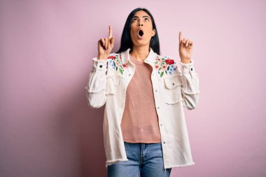 Pembe arka planda gündelik süveter giyen genç ve güzel İspanyol moda kadını şaşırmış ve şaşırmış bir şekilde başımı kaldırıp parmaklarımı ve kollarımı kaldırdım..