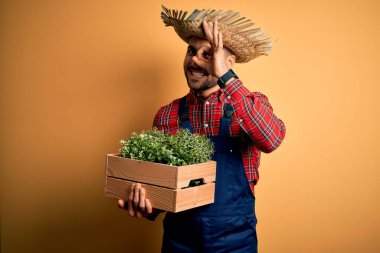 Kırsal kesimdeki genç çiftçi şapkalı ve elinde gülen yüzlü yeşil organik bitki var.