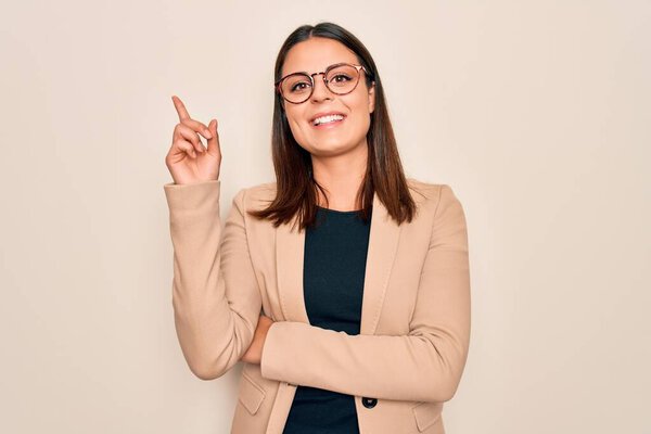 Young beautiful brunette businesswoman wearing jacket and glasses over white background with a big smile on face, pointing with hand and finger to the side looking at the camera.